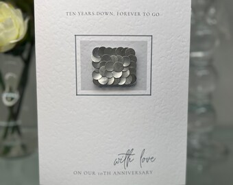 May include: A white card with the text "Ten Years Down, Forever to Go" and "with love" on our 10th Anniversary. A silver circle design is in the centre of the card.