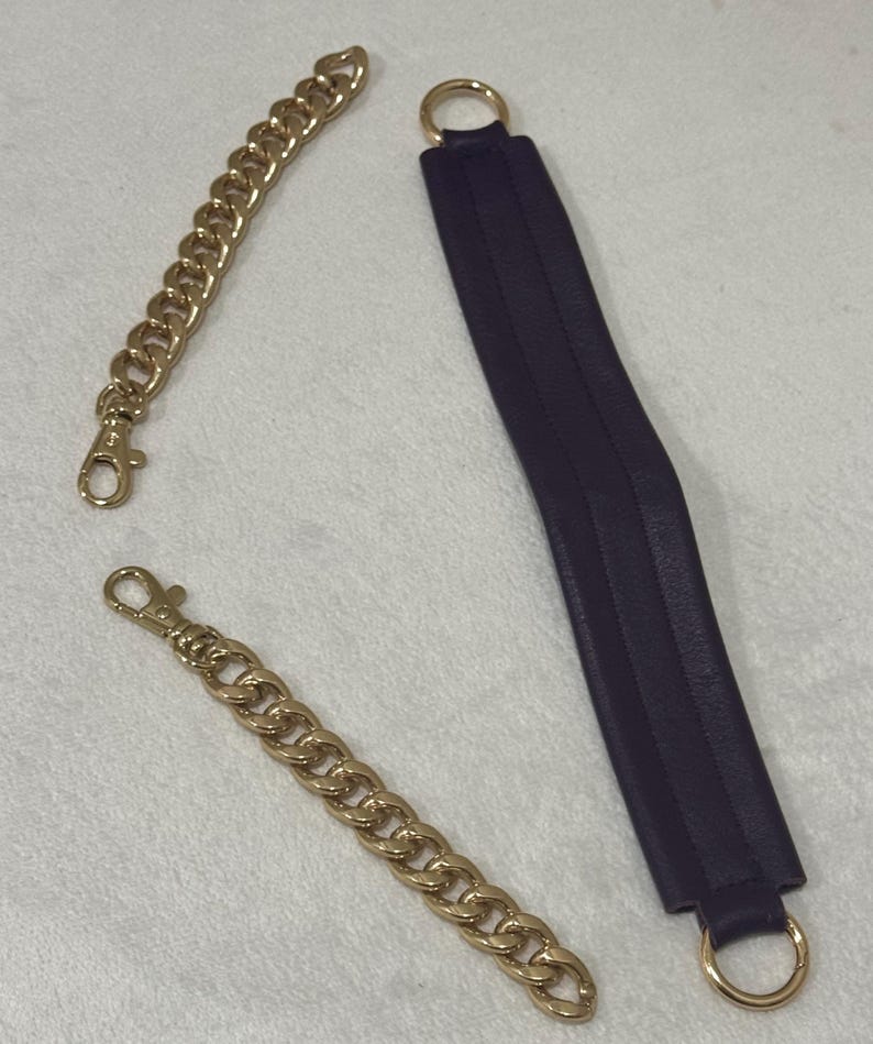 May include: A set of bag accessories including two gold-toned metal chain straps with lobster claw clasps and one long, rectangular dark purple leather strap featuring a gold-toned metal ring attached to each end for secure attachment.