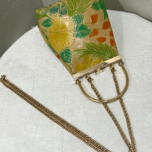 May include: A vintage handbag with a gold chain strap and a gold handle. The bag features a floral pattern with yellow hibiscus flowers, green leaves, and orange accents on a tan background. The bag has a rectangular shape.