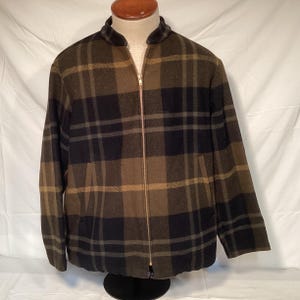 Könnte beinhalten: Eine Jacke mit Reißverschluss und einem Karomuster in Dunkelolivgrün, Schwarz und Beige. Das Kleidungsstück hat einen Stehkragen, lange Ärmel und einen durchgehenden Metallreißverschluss in der Mitte. Zwei vertikale Eingrifftaschen sind sichtbar.