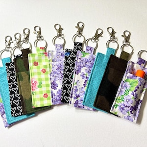 May include: A set of 10 colourful fabric keychains with silver key rings. The keychains are made of different patterned fabrics, including floral, geometric, and plaid designs.