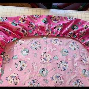 May include: Pink fitted sheet with a cartoon print of two characters holding hands. The print features hearts, bows, and the text "Friendship is our Magic".