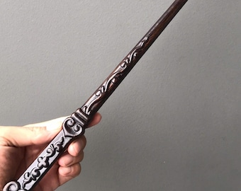 May include: A dark brown wooden wand with intricate carvings. The wand has a rounded tip and a detailed handle with a floral design.