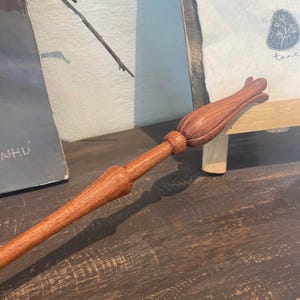 May include: A wooden wand with a carved flower design at the top. The wand is brown and has a smooth finish.