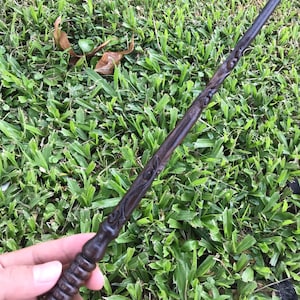 May include: A dark brown wooden wand with intricate carvings. The wand has a rounded tip and a textured handle.