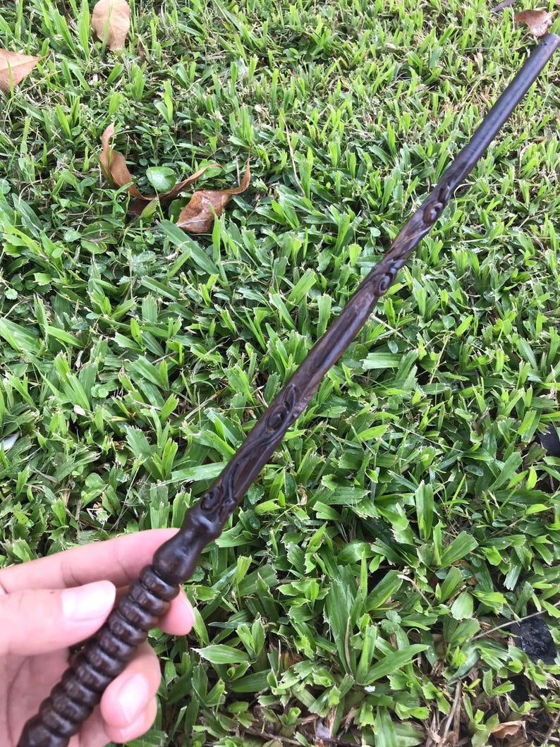 May include: A dark brown wooden wand with intricate carvings. The wand has a rounded tip and a textured handle.