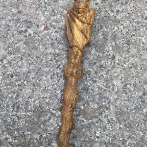 May include: A wooden wand with a carved bat at the top. The wand is brown and has a twisted design.