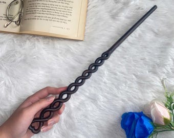 May include: A dark brown wooden wand with a braided design. The wand is held in a hand against a white fluffy background.