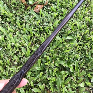 May include: A dark brown wooden wand with intricate carvings. The wand is approximately 33 cm long and has a pointed tip.