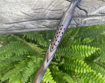 May include: A dark brown wooden wand with a unique design featuring a series of holes and a rounded tip.
