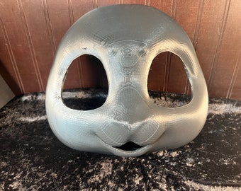 May include: A gray, unpainted, 3D printed animal mask with two eye holes and a mouth hole. The mask is made of a smooth, textured plastic.