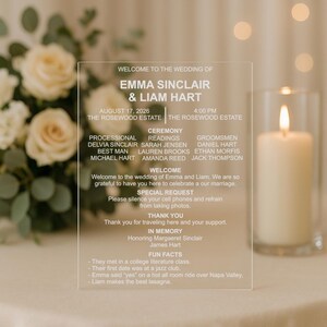 May include: Clear acrylic wedding sign with white text. The sign lists the names Emma Sinclair & Liam Hart, the date, time, and location of the wedding. It also includes the wedding party, ceremony details, and a welcome message.