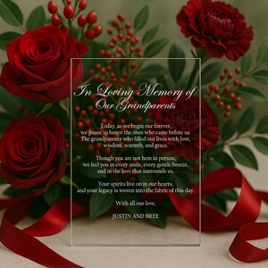 May include: A clear acrylic memorial plaque with the text "In Loving Memory of Our Grandparents" surrounded by red roses, carnations, and berries. A red ribbon is draped across the bottom. The text includes a heartfelt message.