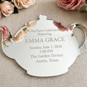 May include: A mirrored acrylic teapot-shaped invitation for a tea party. The invitation includes the text "A Tea Party Celebration Honoring EMMA GRACE" and event details: Sunday, June 7, 2026, 1:00 PM, The Garden Terrace, Austin, Texas.