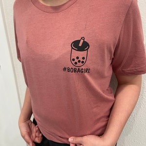 May include: A pink t-shirt with a black graphic of a boba tea cup and the text "#BOBAGIRL" printed on the front.