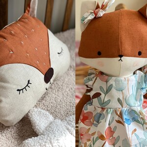 May include: Two plush fox toys. One is a flat pillow with a brown face and closed eyes. The other is a standing fox wearing a white dress with a floral pattern.