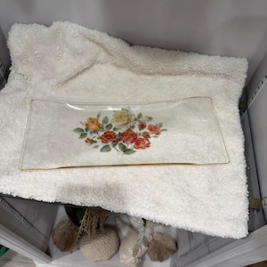 May include: A rectangular glass serving tray with a floral design. The tray features a gold trim and a central arrangement of red, orange, and yellow roses with green leaves. The tray is resting on a white, fluffy surface.