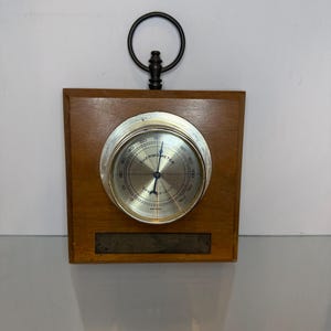 May include: A square wooden wall-mounted thermometer with a circular silver-toned dial face. The dial features the text "THERMOMETER" and "SPRINGFIELD" with a blue needle. A dark metal ring is attached to the top for hanging purposes.