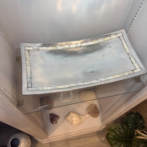 May include: A rectangular silver-toned metal tray featuring a smooth, reflective center surface framed by a border of small, iridescent, square-shaped mother-of-pearl tiles. The tray has slightly curved edges and a polished, metallic finish.