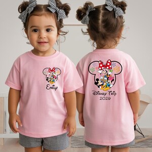 A young girl wearing a pink t-shirt with a Disney character design and the text "Disney Trip 2020" printed on the back.