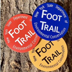 May include: Three round stickers with the text "New York State Department of Environmental Conservation Foot Trail" in white lettering on a blue, red, and yellow background.
