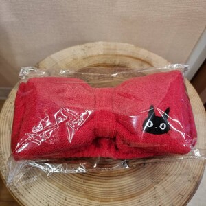 May include: Red headband with a black cat design. The headband is made of a soft, plush material and is in a bow shape.