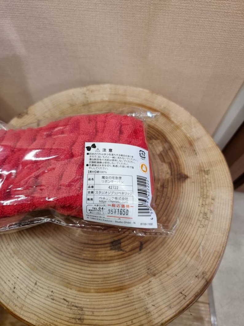 May include: Red cotton hair ribbon with the text "魔女の宅急便" (Majo no Takkyubin) and "リポンターパン" (Ribon Ta-pan) on the packaging. The ribbon is packaged in a clear plastic bag with a label that includes the product name, number, and price.