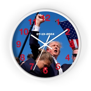 Könnte beinhalten: Weiße Wanduhr mit blauem Zifferblatt mit politischem Bild. Das Zifferblatt hat rote Zahlen und weiße Zeiger. Das Datum "07-13-2024" ist auf dem Zifferblatt aufgedruckt.