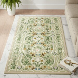 May include: A rectangular, light green rug with a floral pattern. The rug features a repeating design of stylized flowers and foliage in shades of green, yellow, and blue. The rug is placed on a marble surface, with a sofa and a potted fern in the background.