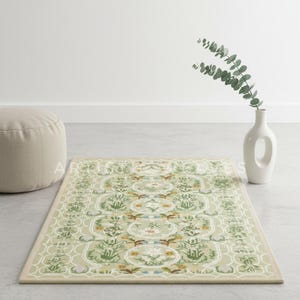 May include: A rectangular, light green rug with a detailed floral and geometric pattern. The rug features a beige border and is placed on a gray surface. A white vase with greenery and a beige ottoman are in the background.