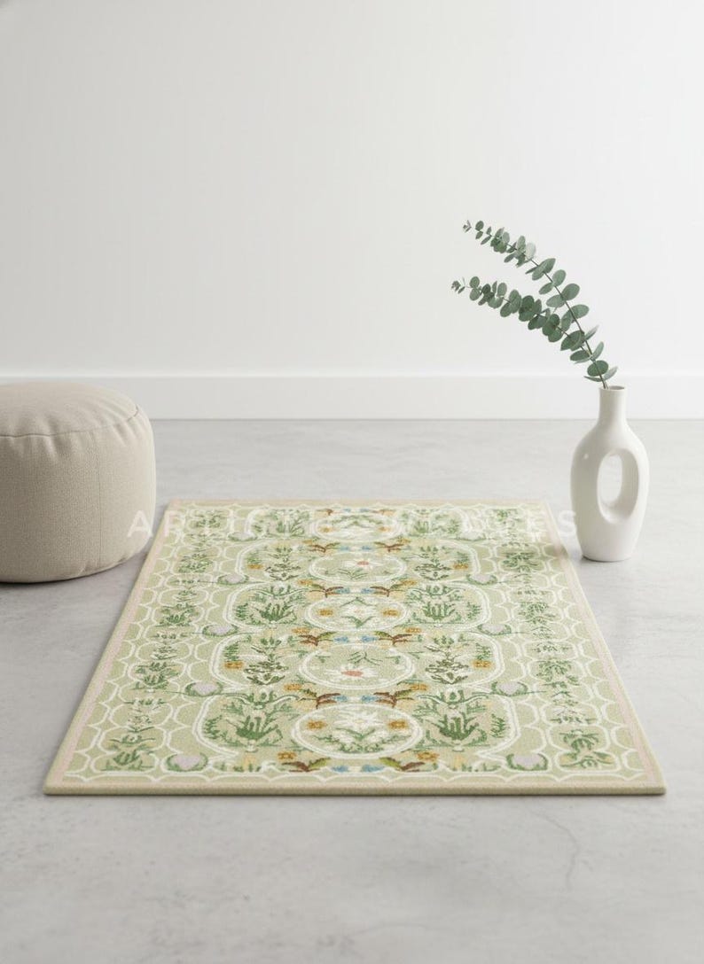May include: A rectangular, light green rug with a detailed floral and geometric pattern. The rug features a beige border and is placed on a gray surface. A white vase with greenery and a beige ottoman are in the background.