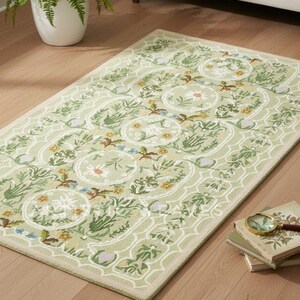 May include: A rectangular, light green rug with a floral pattern. The rug features a repeating design of circular floral medallions and botanical elements in shades of green, yellow, and brown. The rug is placed on a hardwood floor.