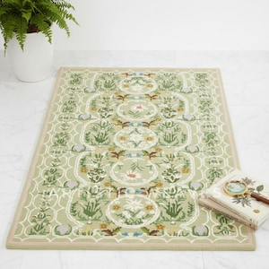 May include: A rectangular rug with a light green background and a floral pattern in shades of green, white, yellow, and brown. The rug has a pink border and a beige edge. A potted fern and books with a magnifying glass are in the background.