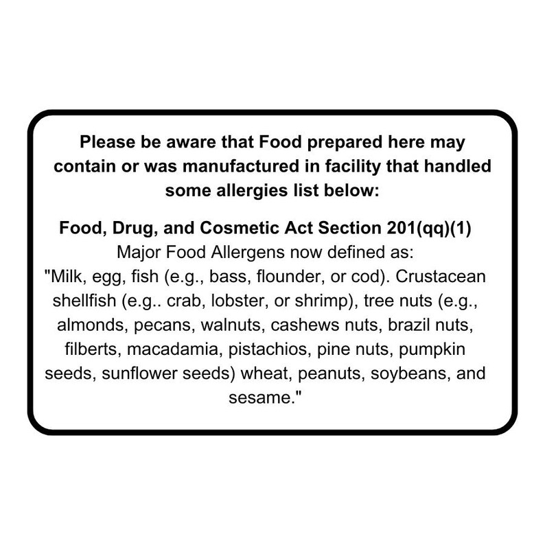 May include: Black and white sign with the text "Please be aware that Food prepared here may contain or was manufactured in facility that handled some allergies list below: Food, Drug, and Cosmetic Act Section 201(qq)(1) Major Food Allergens now defined as: "Milk, egg, fish (e.g., bass, flounder, or cod). Crustacean shellfish (e.g.. crab, lobster, or shrimp), tree nuts (e.g., almonds, pecans, walnuts, cashews nuts, brazil nuts, filberts, macadamia, pistachios, pine nuts, pumpkin seeds, sunflower seeds) wheat, peanuts, soybeans, and sesame."