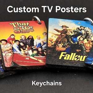 May include: Four square keychains with TV show posters: "One Piece", "That '70s Show", "Fallout", and "Star Trek: The Next Generation". Each keychain has a silver ring. The text "Custom TV Posters" and "Keychains" are visible.