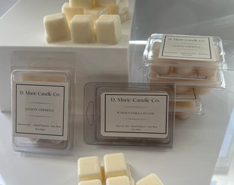 May include: Several packages of wax melts from D. Marie Candle Co. are displayed. The wax melts are in the shape of small cubes and are a creamy off-white color. The labels read "Lemon Verbena" and "Warm Vanilla Sugar".