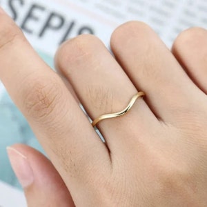 May include: A simple gold band ring with a curved, wave-like design.