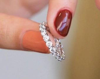May include: A silver band ring with a row of small, clear round stones.