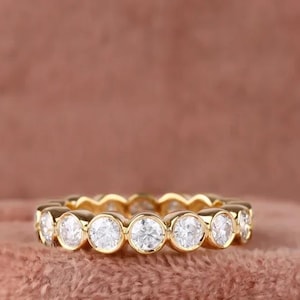 Op de afbeelding: Een gouden ring met een rij ronde, bezel-gezet diamanten.