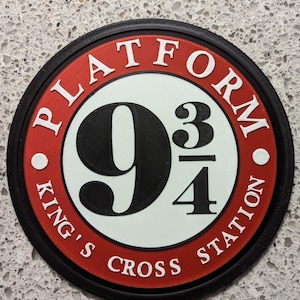 May include: A circular sign featuring a red border with the white text PLATFORM and KING'S CROSS STATION. The center is white with the large black number 9 and the fraction 3/4. The entire sign is framed by a thin black outer ring.