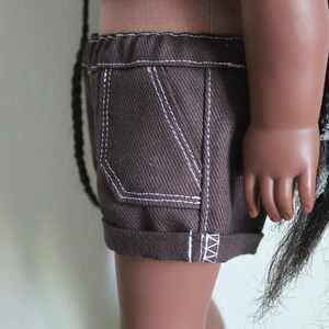 May include: Brown denim shorts with white stitching and a cuffed hem. The shorts have a single front pocket.