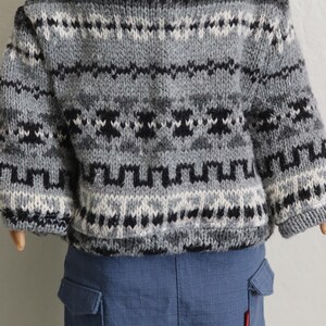 May include: A gray, black, and white patterned sweater with long sleeves. The sweater is worn by a doll and paired with blue cargo pants. The sweater features a geometric design and is made of a knitted material.