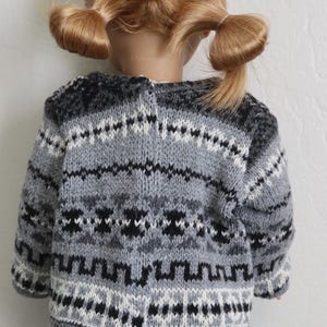 May include: A gray, black, and white patterned sweater on a doll. The sweater has a round neckline and a geometric design. The doll has blonde hair styled in two pigtails.