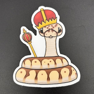 May include: A cartoon snake wearing a gold crown and red robe, holding a scepter. The snake is coiled up and has brown and white scales.