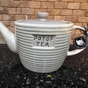 May include: A white ceramic teapot with a ribbed design and a black label that reads "Pot of Tea".
