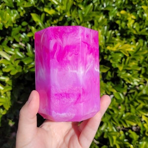 May include: A pink and white resin pen holder with a swirled design. The holder is shaped like a hexagon and has a glossy finish.