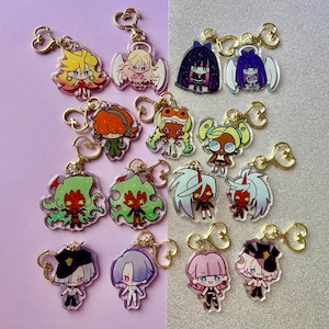 Könnte beinhalten: Eine Sammlung farbenfroher Acryl-Schlüsselanhänger mit Charakterdesigns im Anime-Stil. Jeder Schlüsselanhänger hat einen goldfarbenen herzförmigen Verschluss. Die Charaktere haben einzigartige Frisuren, Outfits und Ausdrücke in verschiedenen Farben.