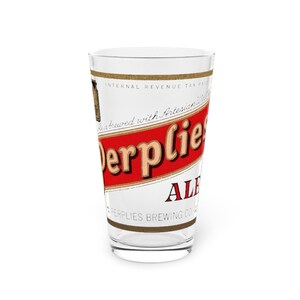 Puede incluir: Un vaso de cerveza transparente con una etiqueta roja y dorada que muestra el texto Derplies ALE y PERPLIES BREWING CO. La etiqueta incluye la frase Internal Revenue Tax Paid y menciona que está elaborado con agua artesiana.