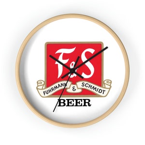 May include: A white round clock with a wood frame features a red square with the letters "F&S" in white. Below the square is a gold banner with the text "FUHRMANN & SCHMIDT" and the word "BEER" in black.