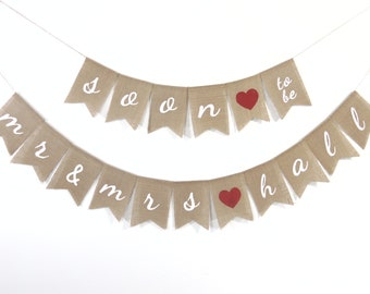 May include: A burlap banner with the text "Mr. & Mrs." and "Soon to be Hall" in white lettering. The banner has red hearts between the words.